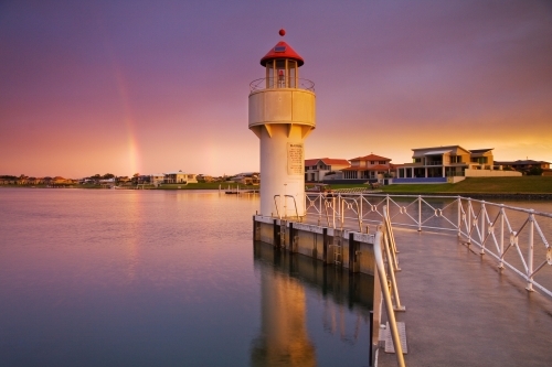 A rainbow in a dark sky over a light beacon at the end of jetty on a river