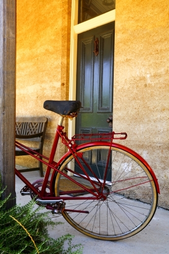 A red bicycle parked against a post outside a cottage entrance.