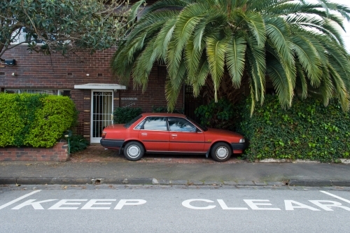 A red car is parked in front of an apartment block next to a keep clear road sign