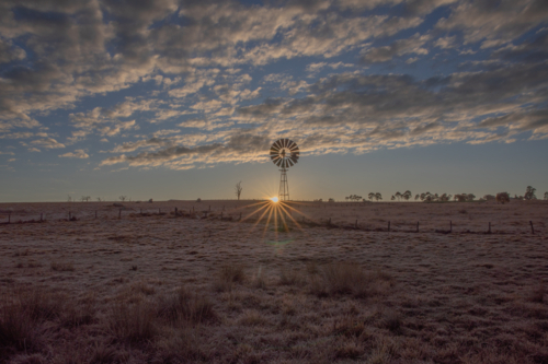 A rising sun, a country windmill and a cloudy sky - Australian Stock Image