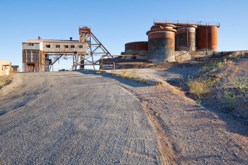 A road leading up to rusted tanks and abandoned buildings of an closed mine