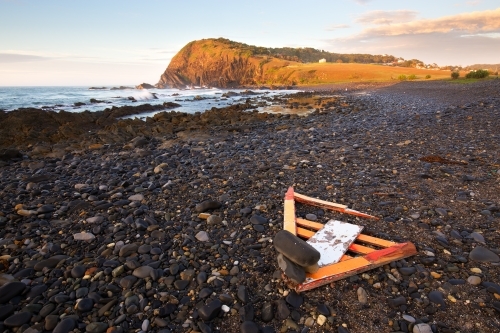 A rocky coastal shoreline with washed up debris and headland in the background