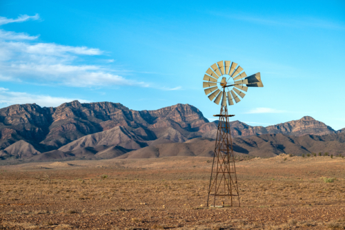 A rustic outback windmill stands before a dramatic mountain range on an arid plain - Australian Stock Image