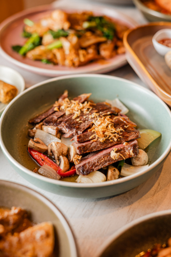 A savoury stir-fried beef dish sits in a bowl, garnished with crunchy onions - Australian Stock Image