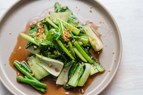 A serving of stir-fried Asian greens sits on a neutral-coloured plate - Australian Stock Image