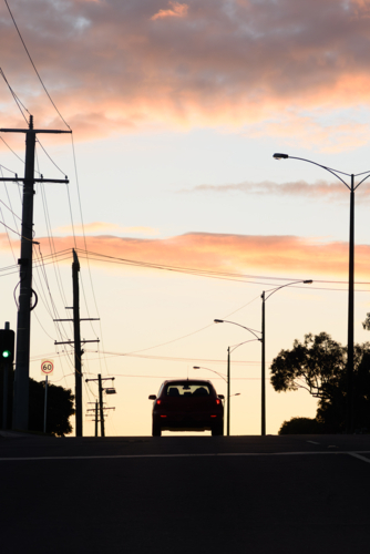 A silhouette landscape at dusk, featuring a car, power poles, and streetlights on the road - Australian Stock Image