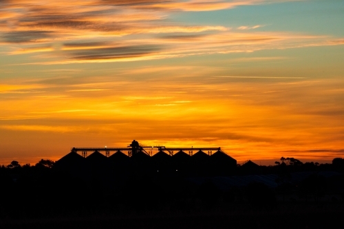 A silhouette of industrial building under the vibrant orange sunset sky with warm hues. - Australian Stock Image