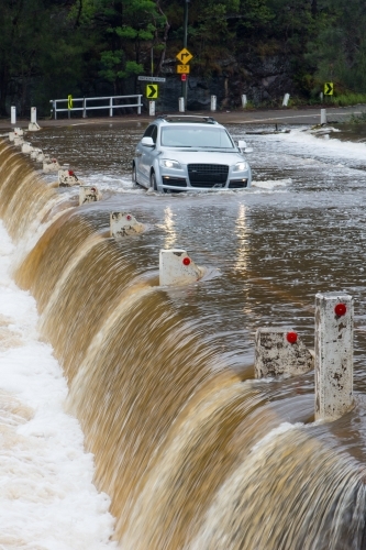 A silver car crossing a flooded weir