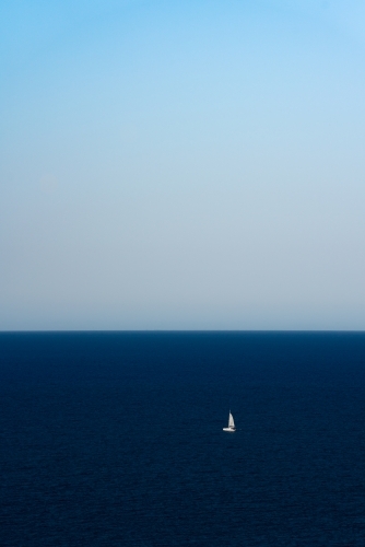 A single sailboat sailing in the middle of the deep blue ocean - Australian Stock Image