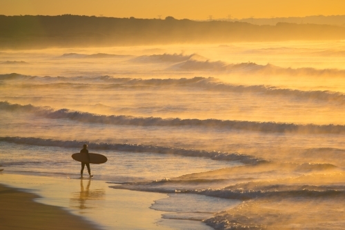 A single surfer heads into the waves at dawn
