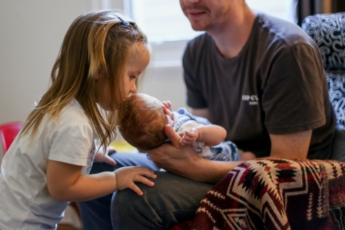 A sister kisses her newborn sibling on the forehead - Australian Stock Image