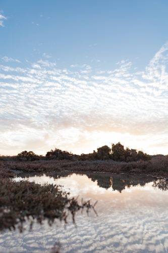A sky with scattered clouds and warm glow of the sun reflecting on the water - Australian Stock Image