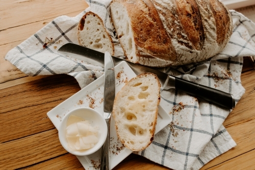 A slice of bread on a white plate with butter with Home made Sour dough bread cooling on a tea towel - Australian Stock Image