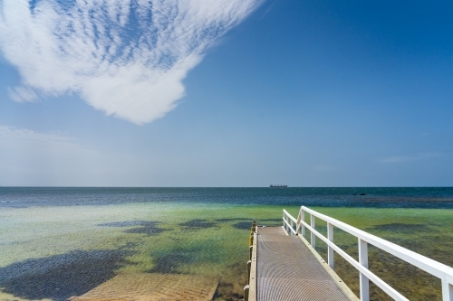 A small coastal jetty leading out over shallow water under an unusual cloud formation - Australian Stock Image
