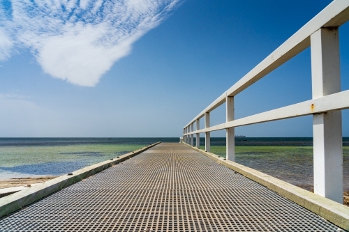 A small coastal jetty leading out over shallow water under an unusual cloud formation - Australian Stock Image