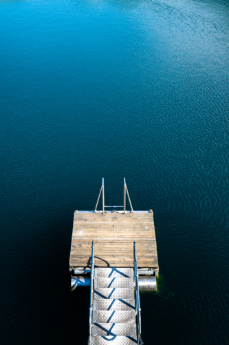 A small wooden dock extends into calm, deep blue lake water - Australian Stock Image