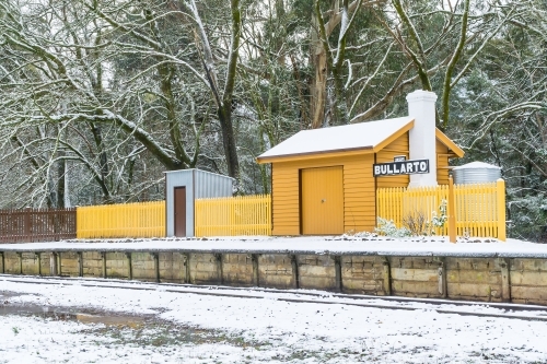 A small yellow railway station on a platform covered in snow