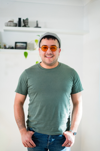 A smiling man in his 30s wears sunglasses and a T-shirt in a bright room. - Australian Stock Image