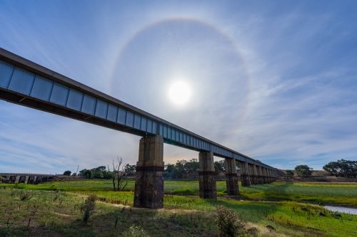 A Solar Halo low in the sky over a railway bridge across a river - Australian Stock Image