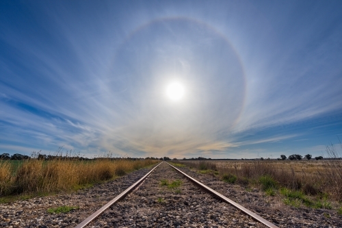 A solar halo low in the sky over receding railway tracks - Australian Stock Image