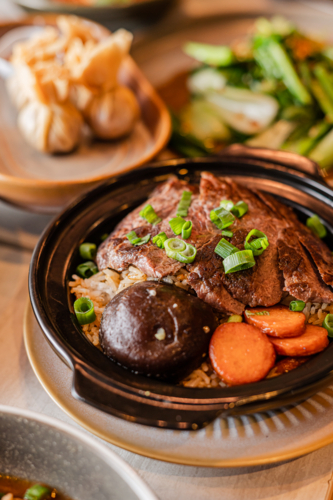 A steaming hot dish showcases tender beef slices topped with green onions, accompanied by vegetables - Australian Stock Image