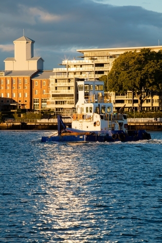 A sunlit tug boat moving upstream along the Brisbane River near Teneriffe - Australian Stock Image