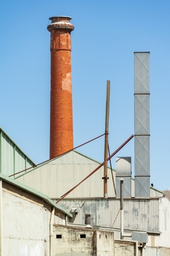 A tall brick chimney beside a large tin factory - Australian Stock Image