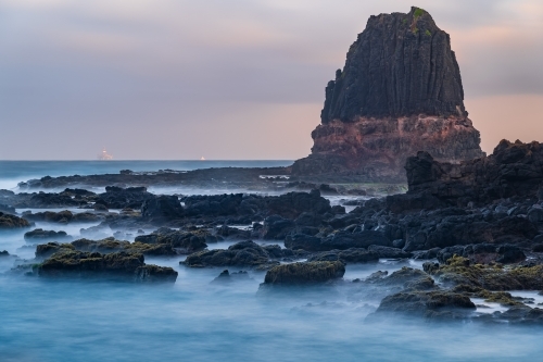 A tall rock formation jutting above a rocky coastline - Australian Stock Image