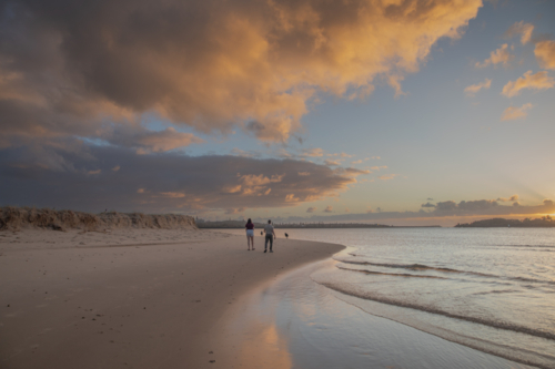 A teenage boy and girl walking on a beach at sunrise under a cloudy sky - Australian Stock Image