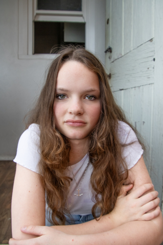 A teenage girl with long hair and a white shirt sitting in a doorway - Australian Stock Image