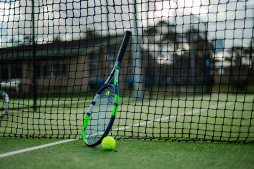 A tennis racquet rests against the net with a ball nearby on an outdoor court - Australian Stock Image