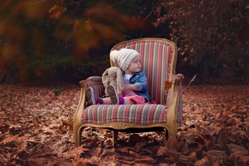 A Toddler Girl Sitting on a Chair amongst Autumn Leaves - Australian Stock Image