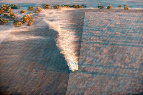 A tractor spreads dust across a wide farmland during cultivation at sunrise. - Australian Stock Image