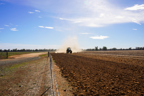 A tractor working the ground in preparation for sowing crops along a fence line - Australian Stock Image