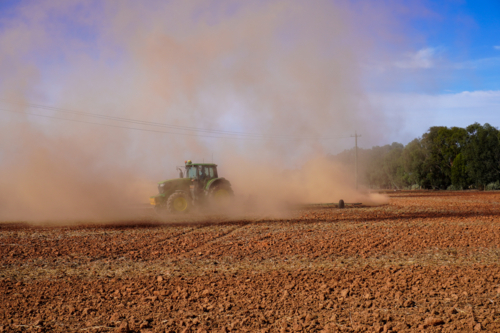 A tractor working the ground in preparation for sowing crops, covered in dust - Australian Stock Image