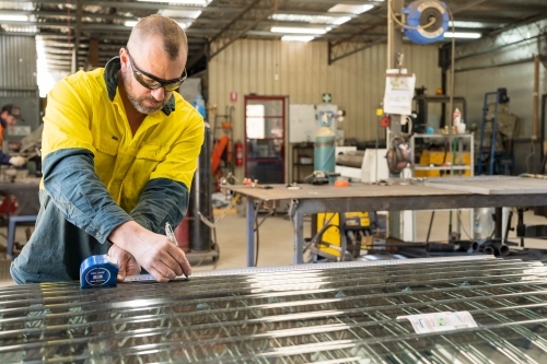 A tradesman measuring and marking screening laid on a workbench - Australian Stock Image