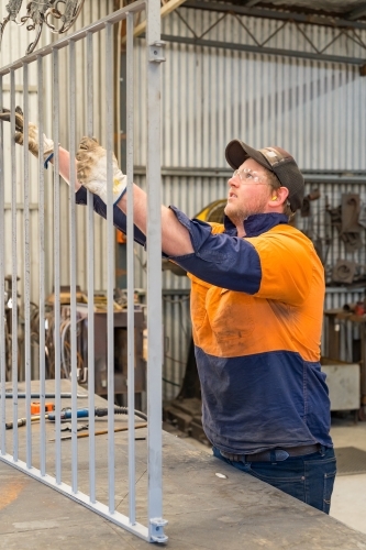 A tradesman wearing high vis clothing holding up a metal gate - Australian Stock Image