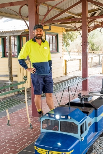 A train driver leaning against the veranda of a model railway station - Australian Stock Image