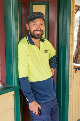 A train driver leaning in the doorway of a railway station smiling - Australian Stock Image