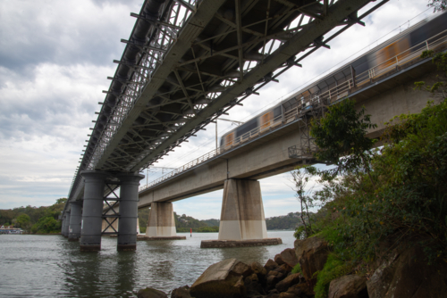 A train going over a concrete rail bridge over the Georges River with the old iron pedestrian bridge - Australian Stock Image