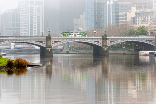 A tram crosses Princes Bridge in morning mist above the Yarra River - Australian Stock Image