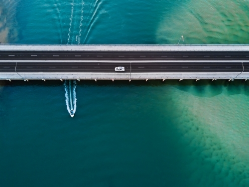 A vehicle drives over the bridge as a speed boat travels underneath leaving a wake behind - Australian Stock Image