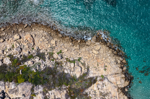 A vibrant aerial view of Rose Bay in Bowen, showcasing its turquoise water and rocky shoreline - Australian Stock Image