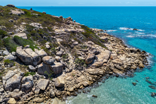 A vibrant aerial view of Rose Bay in Bowen, showcasing its turquoise water and rocky shoreline - Australian Stock Image