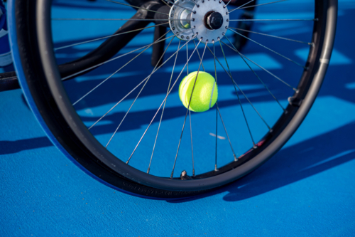 A vibrant yellow tennis ball on a wheelchair on a blue court during a match - Australian Stock Image