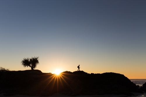A walking hiker is silhouetted on a ridge line by a beautiful bright sunrise.