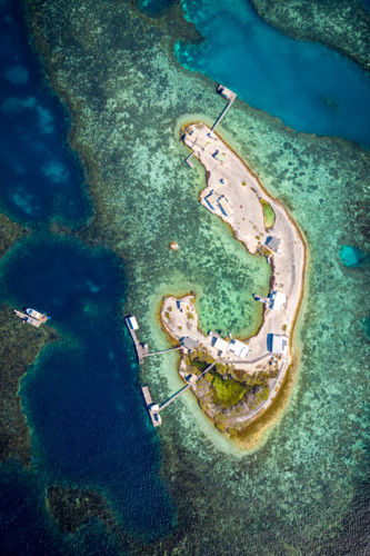 A winding coral cay surrounded by vibrant turquoise shallows and dark reef edges - Australian Stock Image