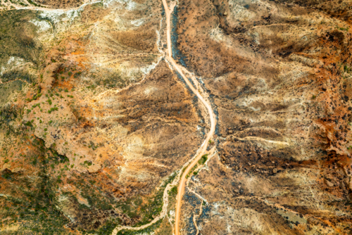 A winding outback track cutting through layered red and brown terrain. - Australian Stock Image