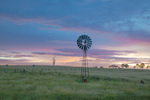 A windmill in a green field underneath a moody dawn skyk - Australian Stock Image