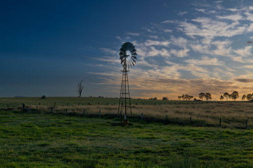 A wispy cloudy sky and a windmill with a silhouette of a tree trunk on an early morning - Australian Stock Image